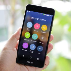A hand holding a smartphone displaying home management apps on the screen.